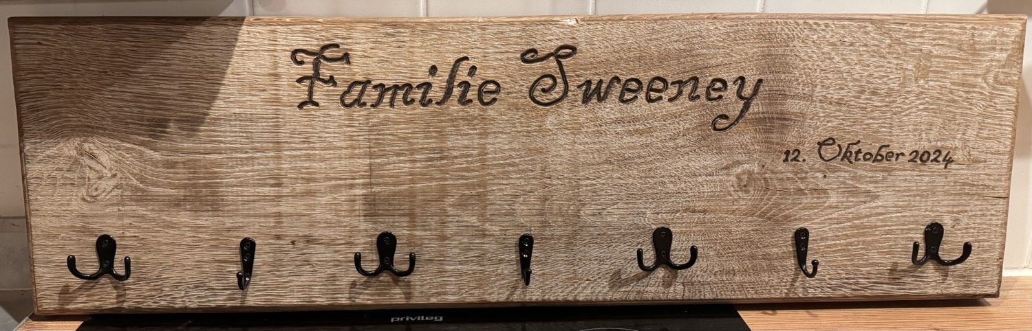Holzgarderobe mit geschnitztem Schriftzug Familie Sweeney und sieben Haken
