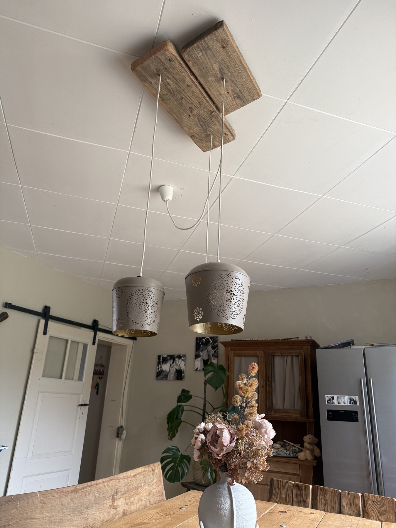 Zwei Holzlatten an der Decke mit zwei gelochten Hängeschirmen über dem Esstisch